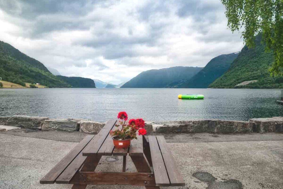 Il lago Hornindalsvatnet Una panchina in legno con sopra un vaso di fiori rossi con sullo sfondo il placido lago Hornindalsvatnet.