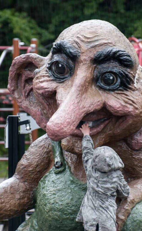 La statua di un troll in cima al monte Fløyen Sopra il monte Fløyen un bambino infila una mano nella bocca aperta di una grossa statua di un troll.