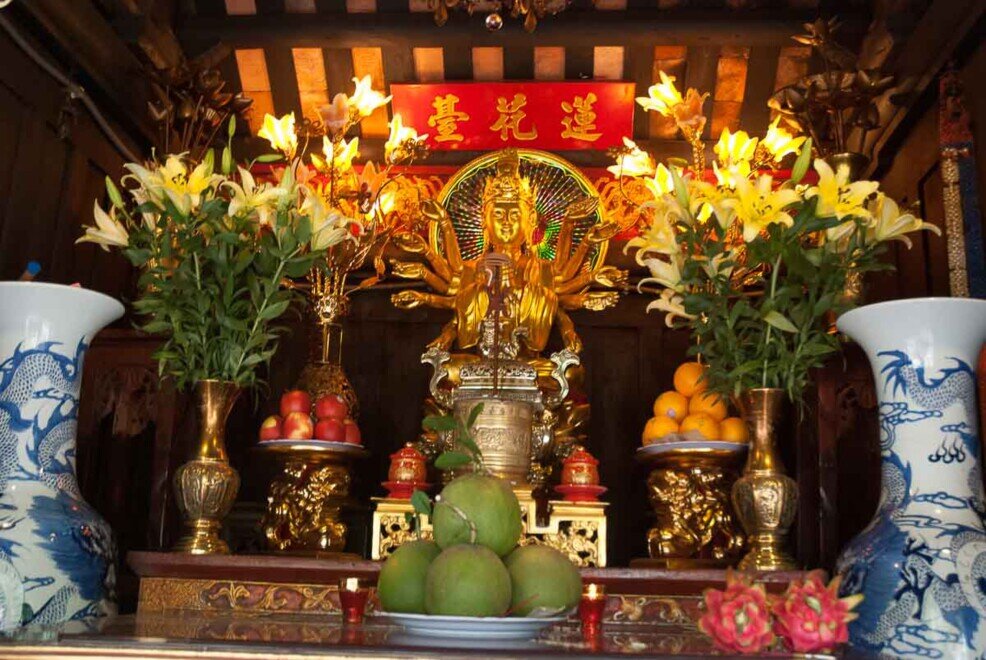Una statua dorata con 8 braccia con intorno addobbi floreali nella Pagoda a Pilastro Unico.