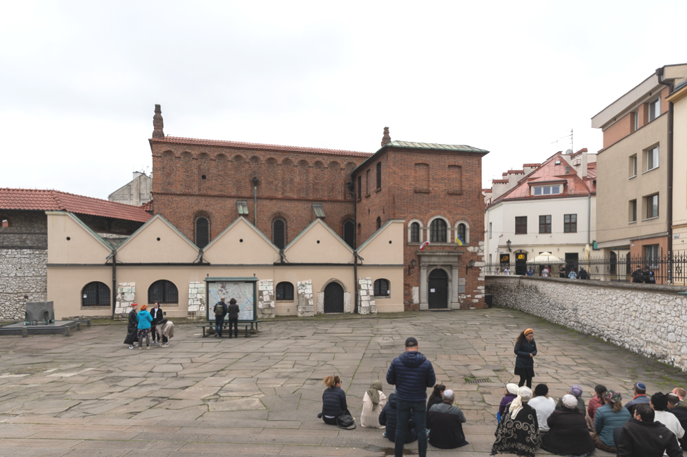 Persone riunite a terra presso la Vecchia Sinagoga di Cracovia, creando un'atmosfera di convivialità e condivisione.