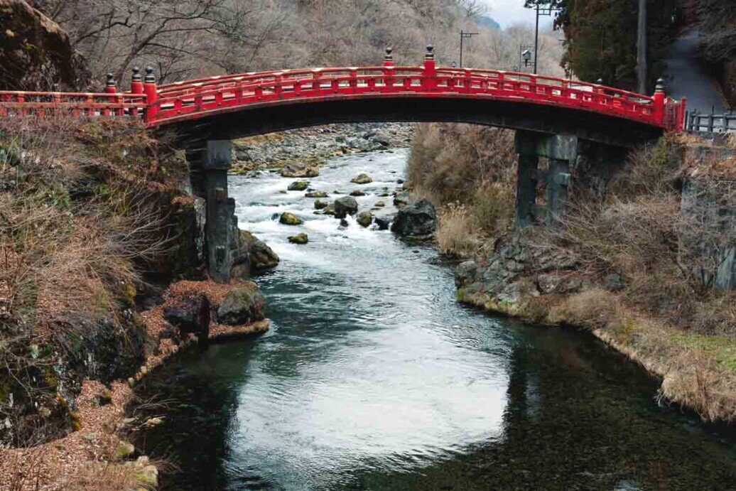 Nikko, il Ponte Shinkyo Ponte Shinkyo di colore rosso sopra un fiume, immerso in un paesaggio montano.