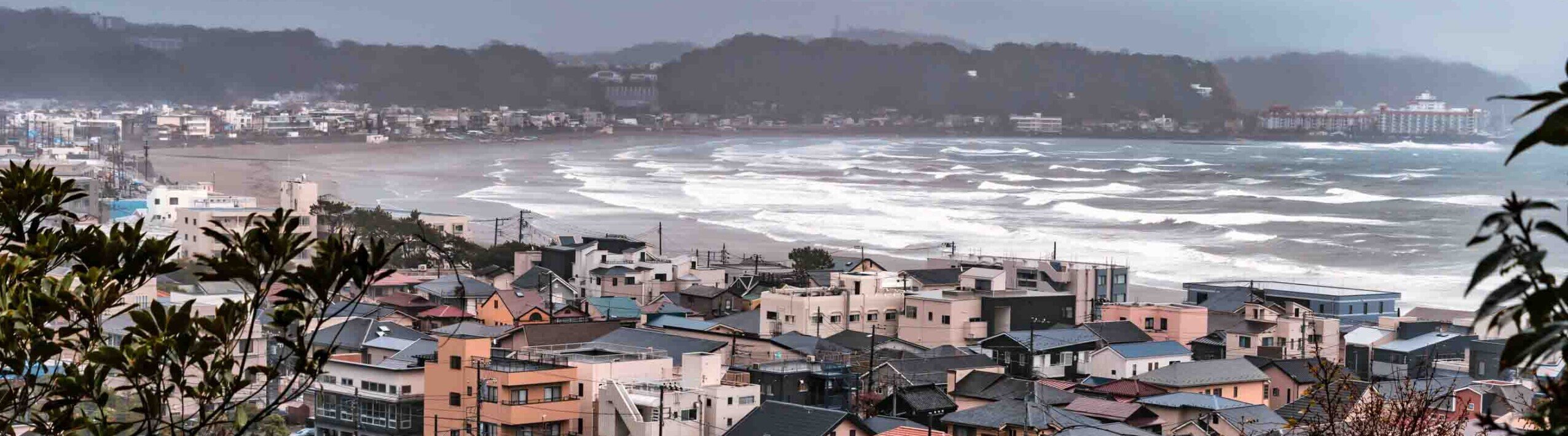 Panorama sulla spiaggia di Kamakura Agglomerato di case dietro una lunga spiaggia con mare mosso
