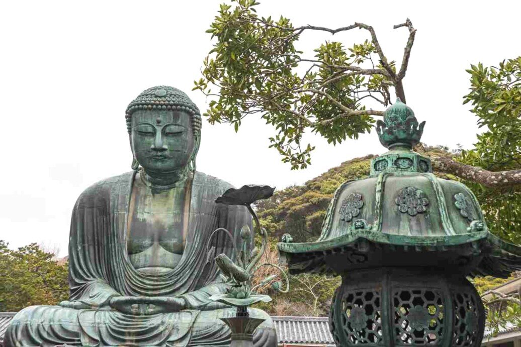 Statua del Grande Buddha di Kotoku-in Statua del Grande Buddha di Kotoku-in seduta accanto a una lanterna, simbolo di pace e illuminazione spirituale.