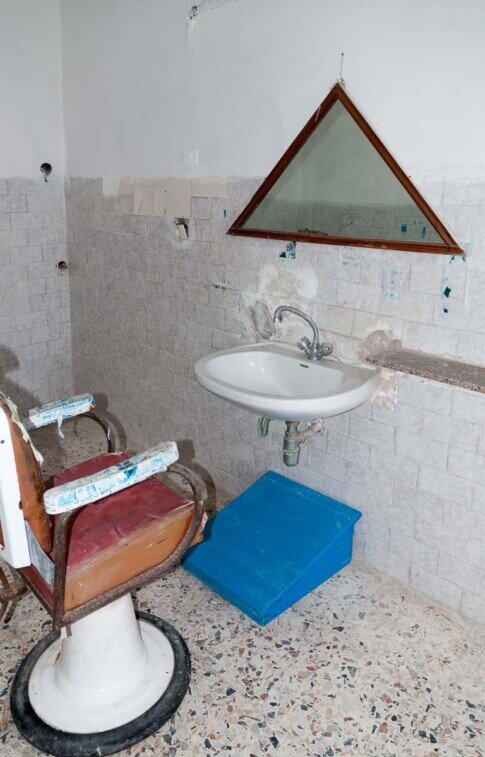 Una vecchio sedile tipico delle barberie, uno specchio triangolare e un lavandino, nel carcere dell'Asinara.