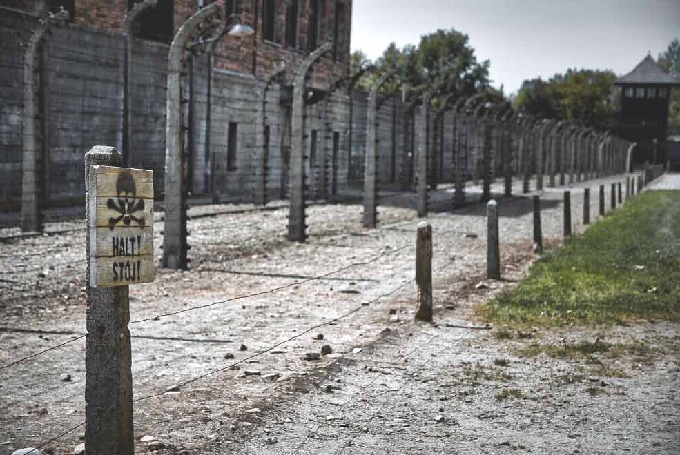 Un cartello con raffigurato un teschio e tanto filo spinato attorno a Auschwitz-Birkenau.