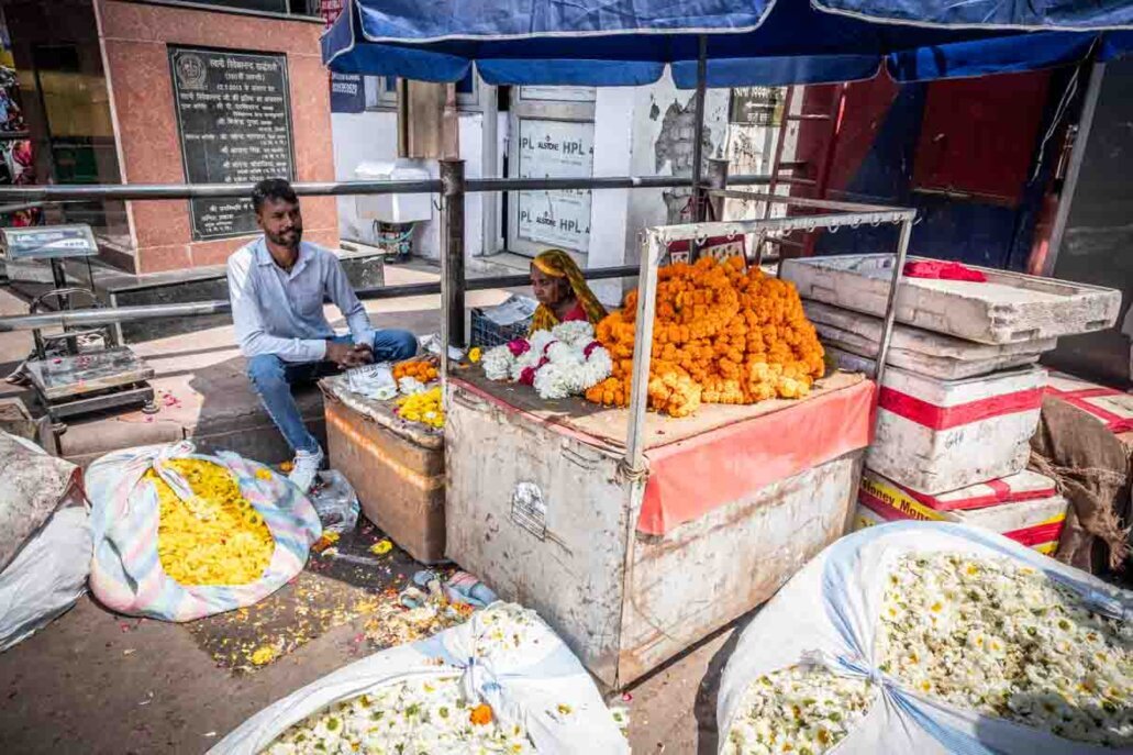 Venditori che offrono Ghirlande di calendula arancioni e gialle, molto usate in India per decorazioni, cerimonie religiose e offerte nei templi.<br />E fiori di gelsomino bianchi.