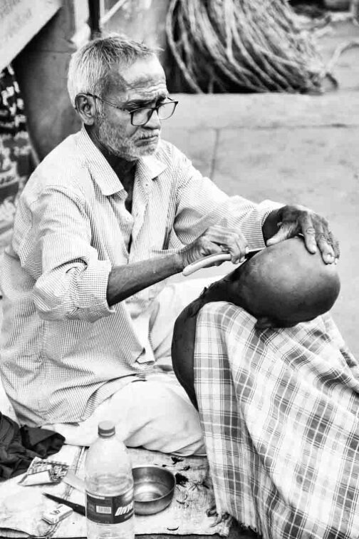 Barbiere effettua rasatura in strada a Varanasi