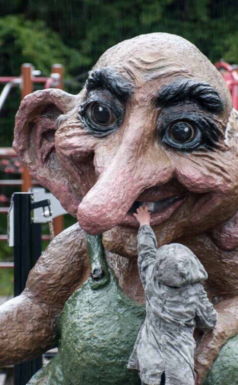 Sopra il monte Fløyen un bambino infila una mano nella bocca aperta di una grossa statua di un troll.
