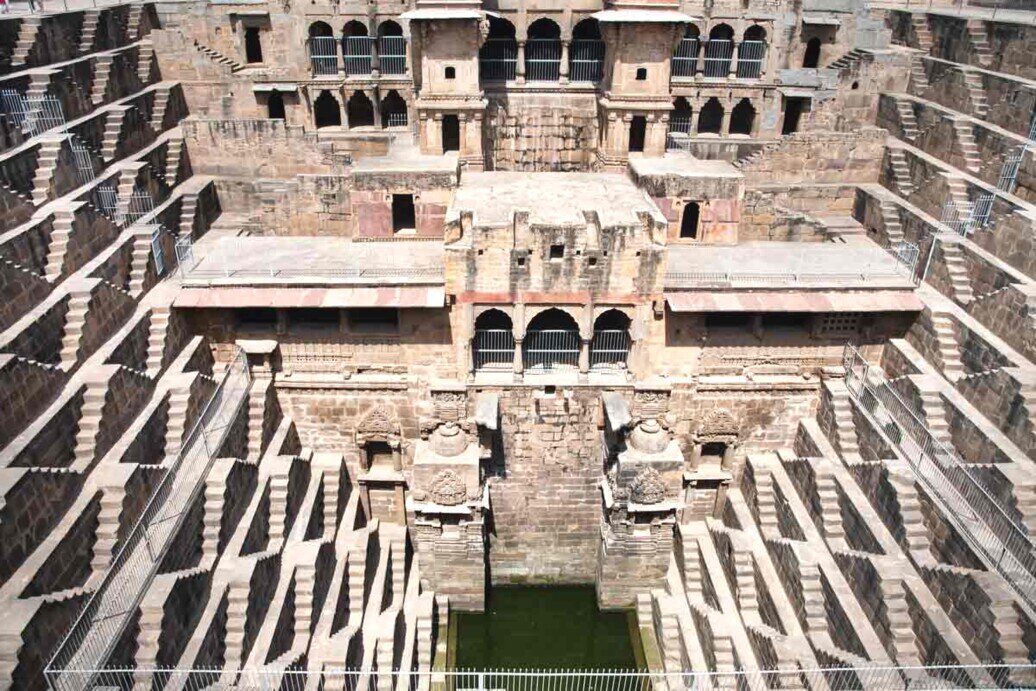 Vista interna di Chand Baori, un grande pozzo a gradini con acqua, caratterizzato da architettura storica.