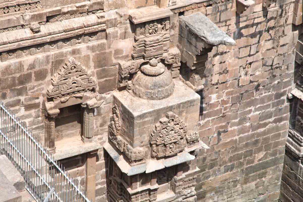 Sculture in pietra sulle pareti del tempio Chand Baori, evidenziando dettagli architettonici intricati.