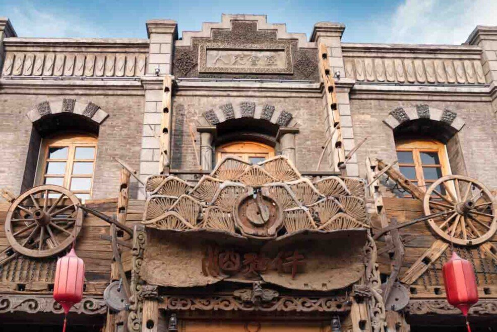 Facciata tradizionale in legno e mattoni con decorazioni rustiche, ruote e lanterne rosse nel centro storico di Pingyao.