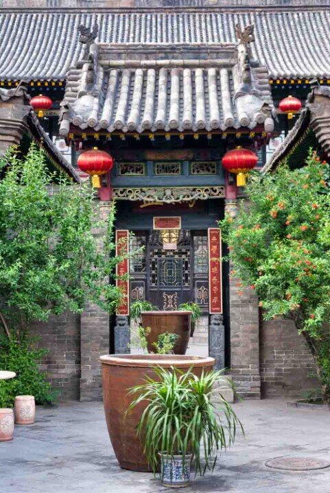 Tipico cortile a Pingyao con vasi di piante e piccolo tetto spiovente con appese lanterne rosse all'ingresso della casa.