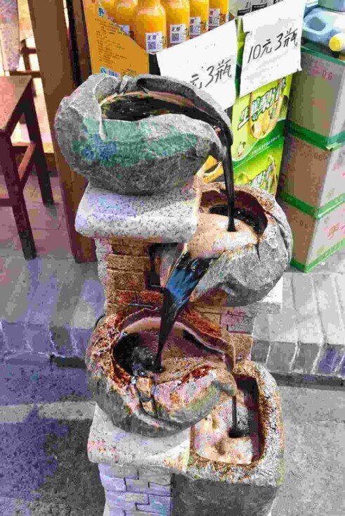 Recipienti in pietra a Pingyao che versano in cascata, uno sull'altro, un liquido scuro, testimonianza del processo tradizionale di produzione dell’aceto di Shanxi.
