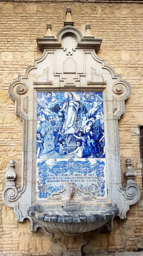 Fontana con pannello in ceramica decorata in stile azulejo blu e bianco, raffigurante una scena religiosa con figure celesti e religiose.