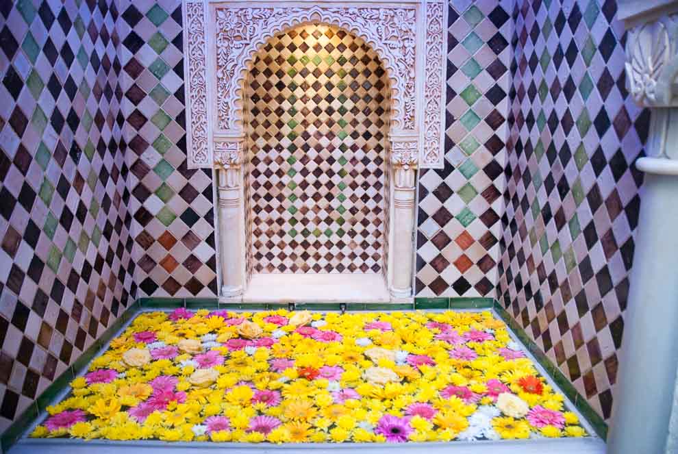 Una fontana adornata con un mosaico di piastrelle colorate in stile moresco con la base riempita di fiori freschi.