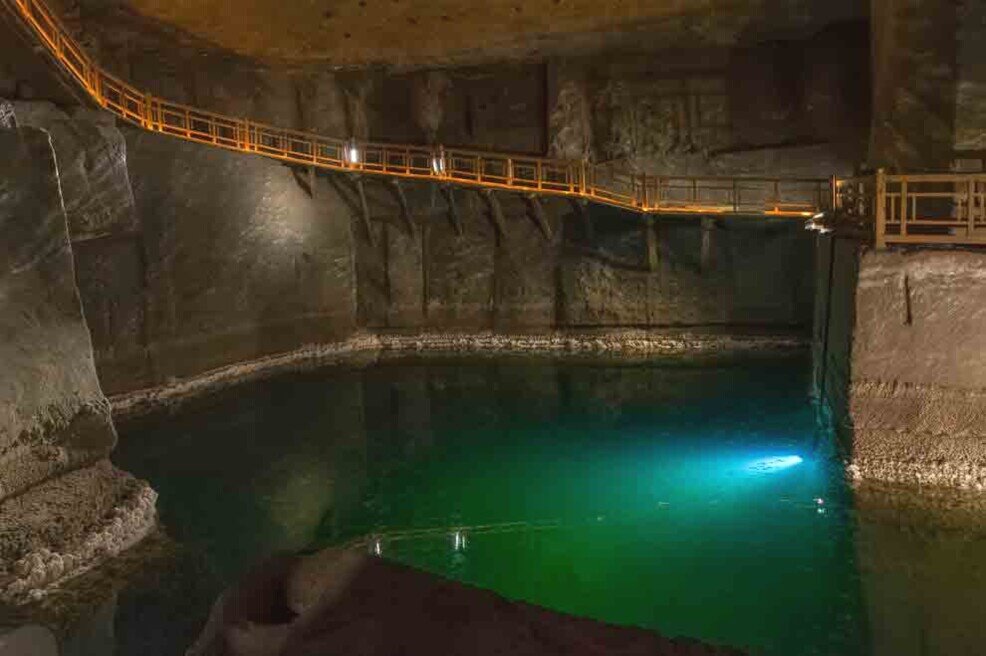 Una cisterna piena di acqua salata col fondo illuminato con una luce verde all'interno della miniera del sale.