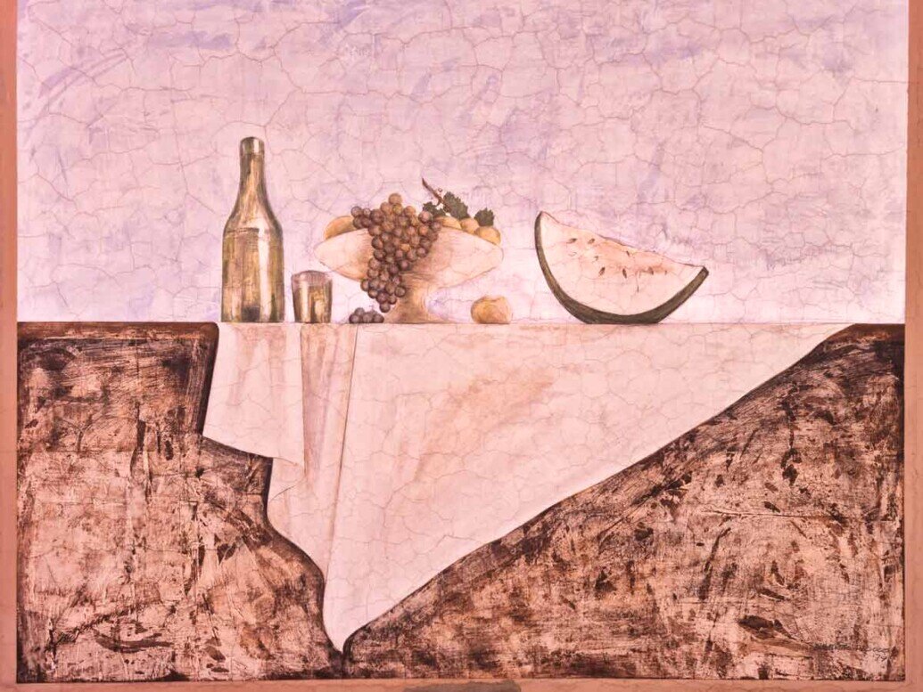 Una tavola coperta da una tovaglia chiara e delle nature morte composte da frutta e bicchiere di vino a simboleggiare i prodotti della terra.