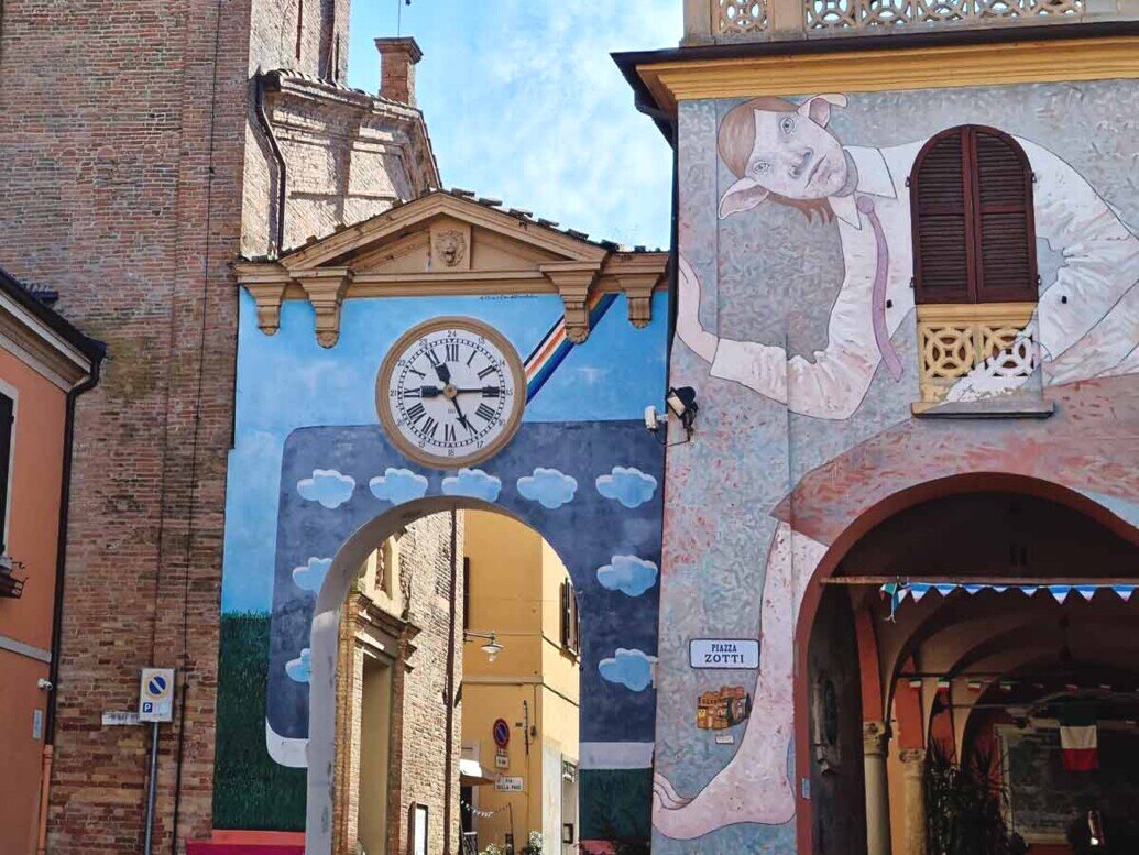 Sulla parete del Comune di Dozza è dipinto uno strano personaggio alieno con grandi orecchie che sembra accogliere i visitatori che attraversano il porticato a fianco.
