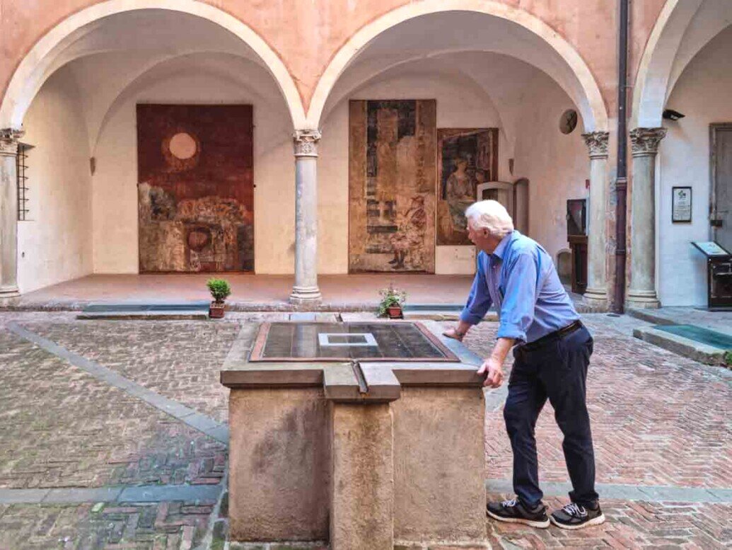 Un uomo appoggiato sul bordo del pozzo osserva gli affreschi nel cortile della Rocca di Dozza.