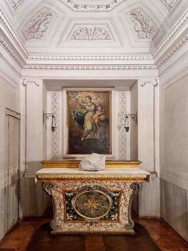 Piccolo altare marmoreo al centro, riccamente decorato con intarsi policromi e simboli religiosi.  Il dipinto sacro sopra l’altare raffigura Santa Barbara protettrice di torri e fortezze