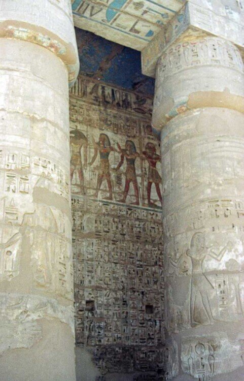 Due colonne con incisioni e il muro dietro con raffigurazioni di feste religiose.