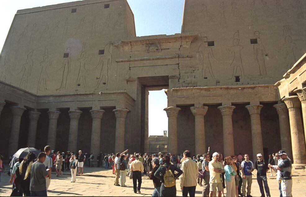 Cortile interno del Tempio di Philae con colonne e rilievi egizi antichi, affollato di turisti sotto il sole.