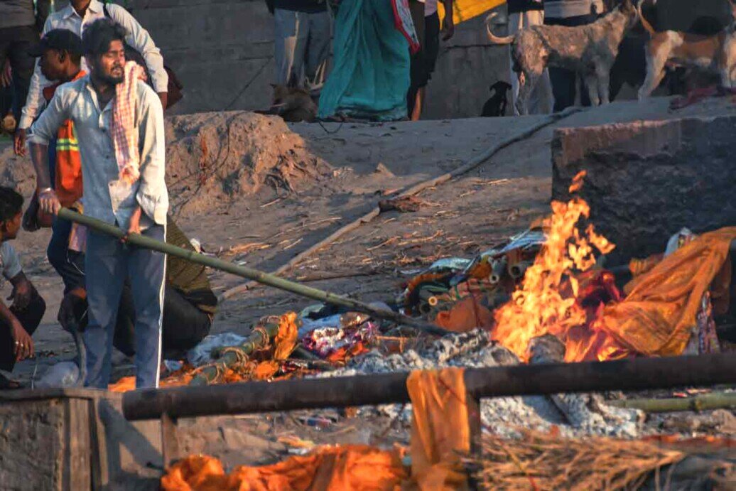 Incenerimento a Varanasi Un uomo si trova accanto a un falò, tenendo un bastone, in un contesto di incenerimento a Varanasi.<br />