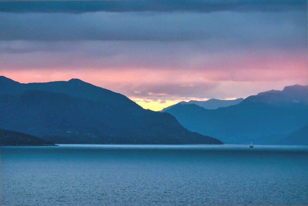 L'alba al Geirangerfjiord All'alba tra le nuvole una luce solare rende il cielo variopinto le montagne scure e il mare blu notte nel Geirangerfjord