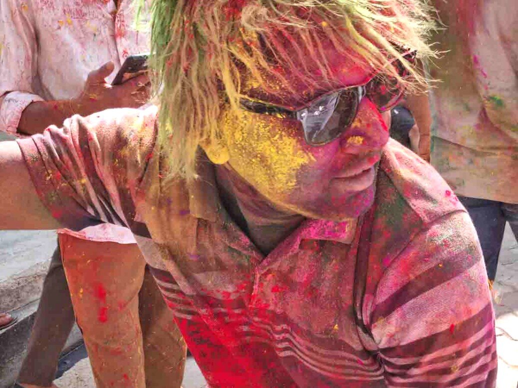 Primo piano di un giovane all'holi festival capelli e viso coloratissimi in un primo piano di un giovane con gli occhiali.