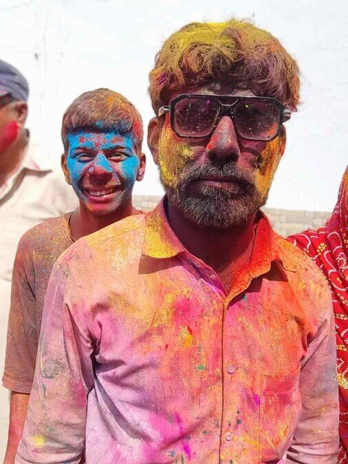 Due ragazzi sporchi di polveri colorate all'holi festival Primo piano serioso di un giovane con gli occhiali e dietro un altro ragazzo che ride divertito mentre vengono fotografati sporchi di polveri colorate.