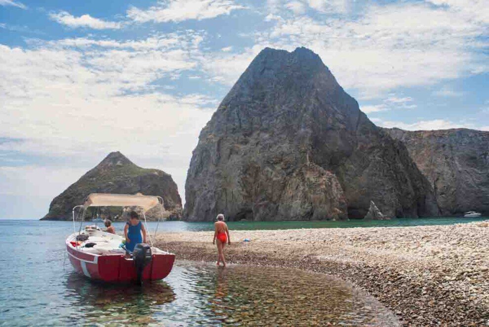 Isola di Palmarola vista dal mare Una barca rossa a motore è approdata su una spiaggia acciotolata con due alti scogli sullo sfondo-nell'Isola di Palmarola.