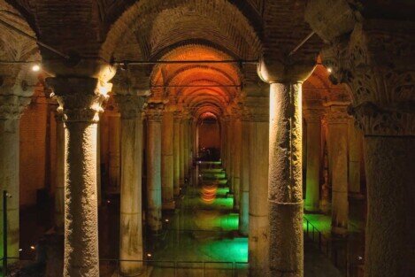 Colonne con capitelli che si perdono in profondità con giochi di luce, il verde che si riflette nell'acqua e il rosso degli archi.