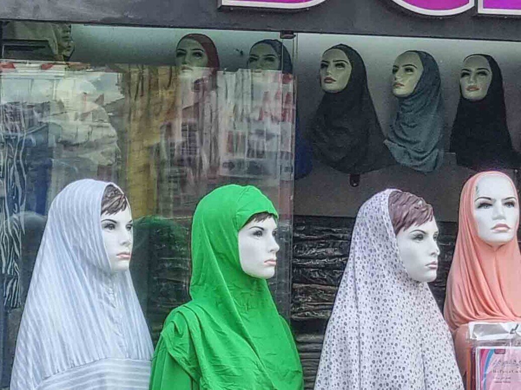 Esposizione di manichini vestiti con indumenti colorati che coprono la testa e lasciano scoperto il viso.