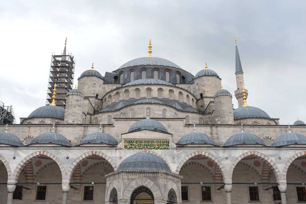 Una moschea con i suoi archi e cupola centrale insieme alle tante cupole di contorno di colore blu.