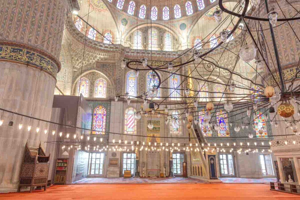 La moschea con il pavimento in moquette rossa, il decorato Mihrab, numerosi lampadari e finestroni che illuminano l'ambiente.