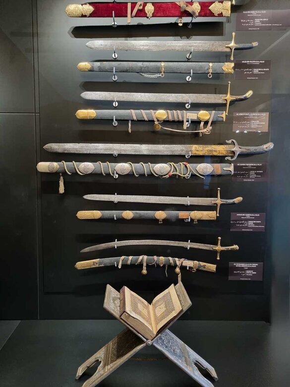 Una serie di spade esposte in verticale con in basso un corano.
