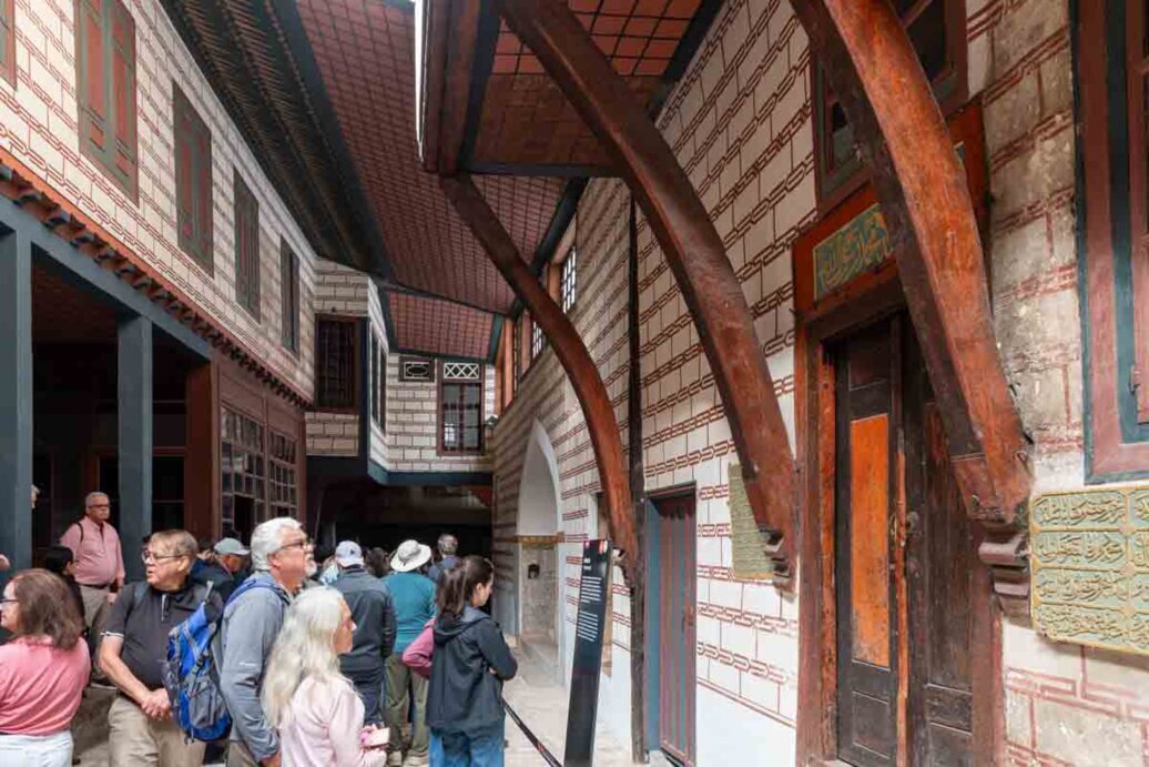 Gruppo di turisti che attraversa un vicolo in un cortile dove sono situati edifici.