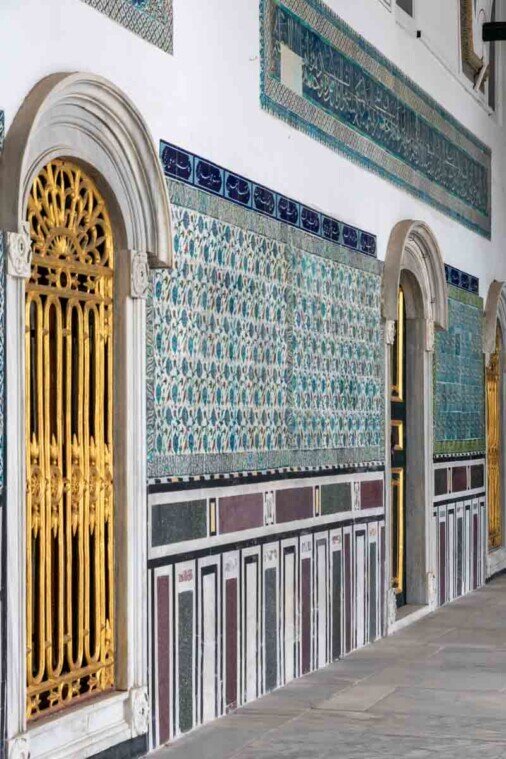 Parete di un cortile interno con porta dorata e parete rivestita da pioastrelle colorate.