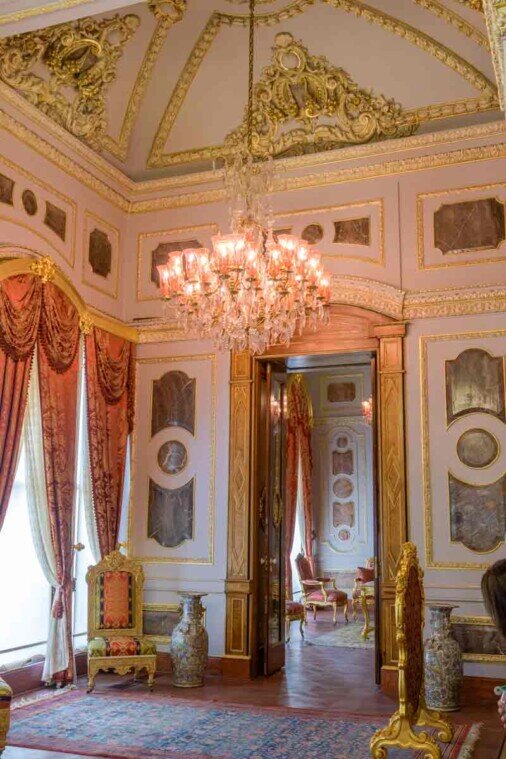 Stanza con cornici dorate, tende rosse e un lampadario a gocce.