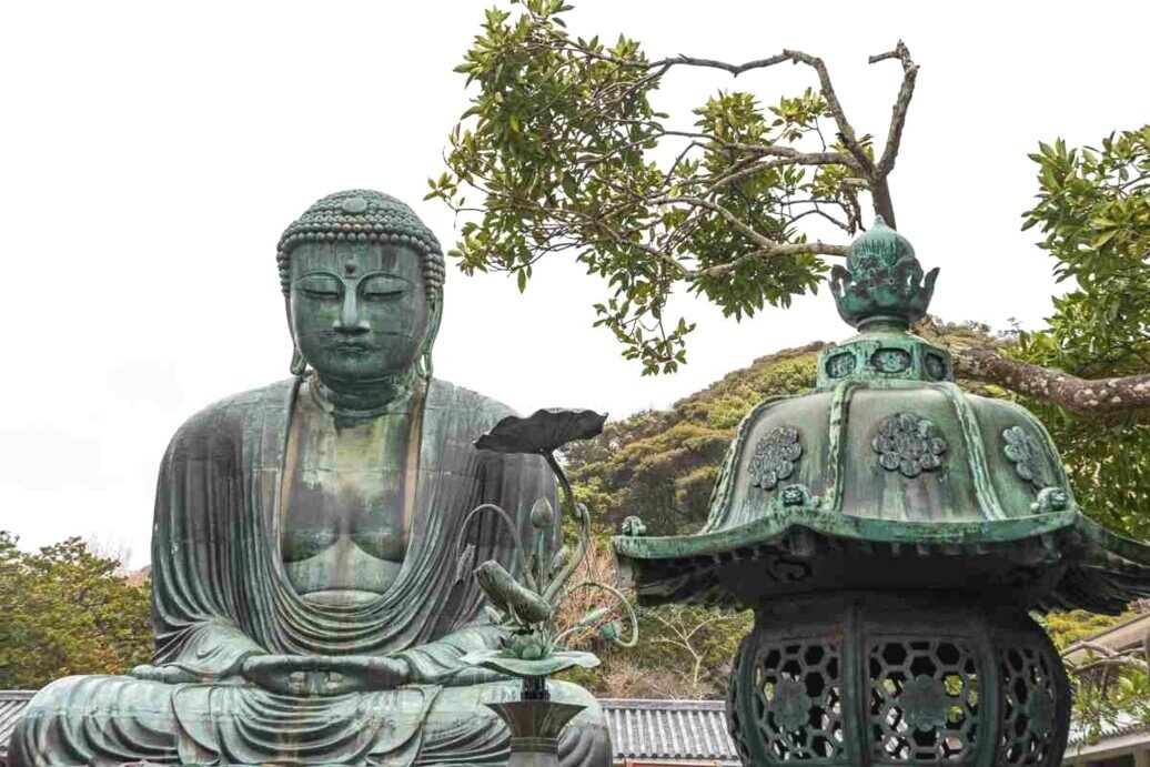 Statua del Grande Buddha di Kotoku-in seduta accanto a una lanterna, simbolo di pace e illuminazione spirituale.
