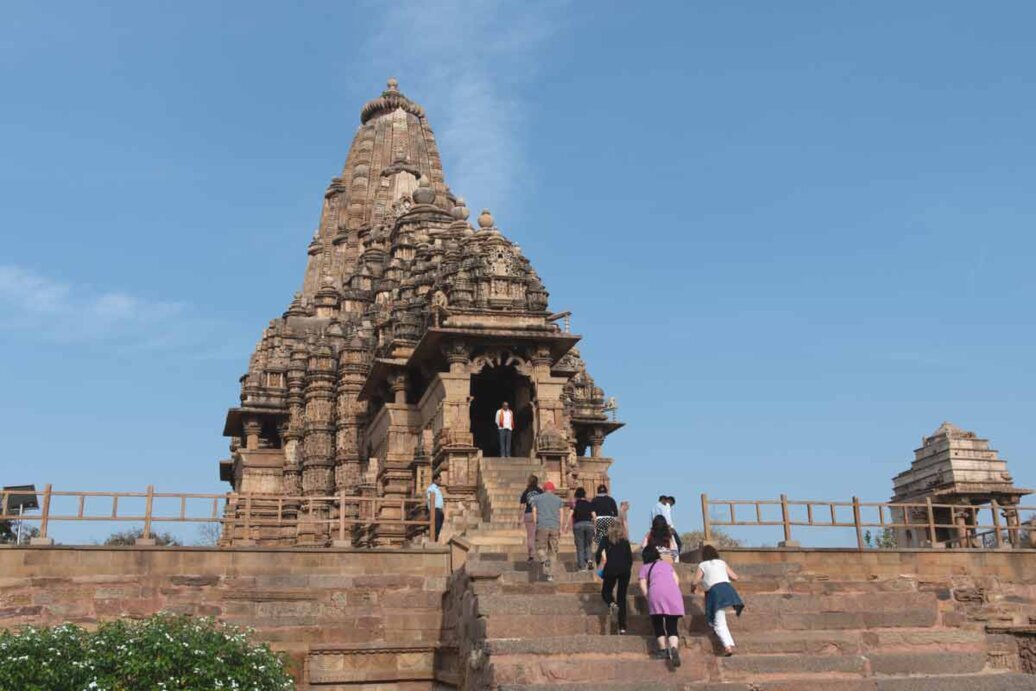 Facciata principale del Tempio Kandariya Mahadeva a Khajuraho, India: maestosa struttura in stile nagara dedicata al dio Shiva, con visitatori che salgono i gradini d'ingresso, esempio iconico dell'architettura templare medievale indiana.