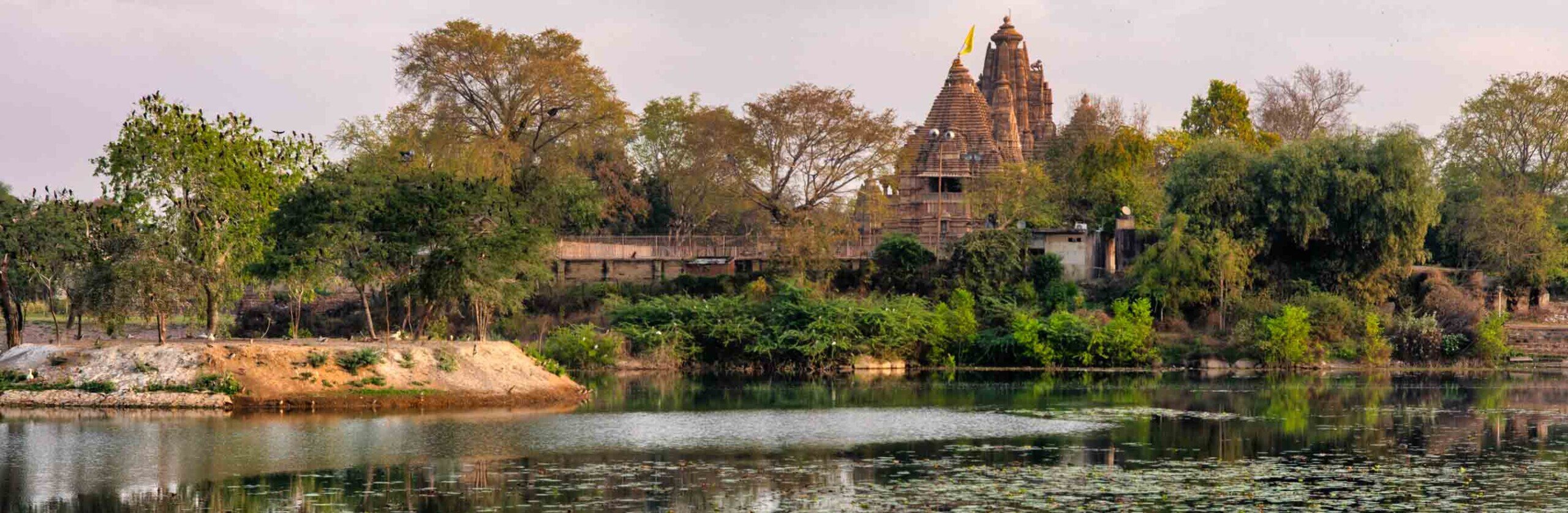 Templi di Khajuraho immersi nel verde e lambiti da un lago.