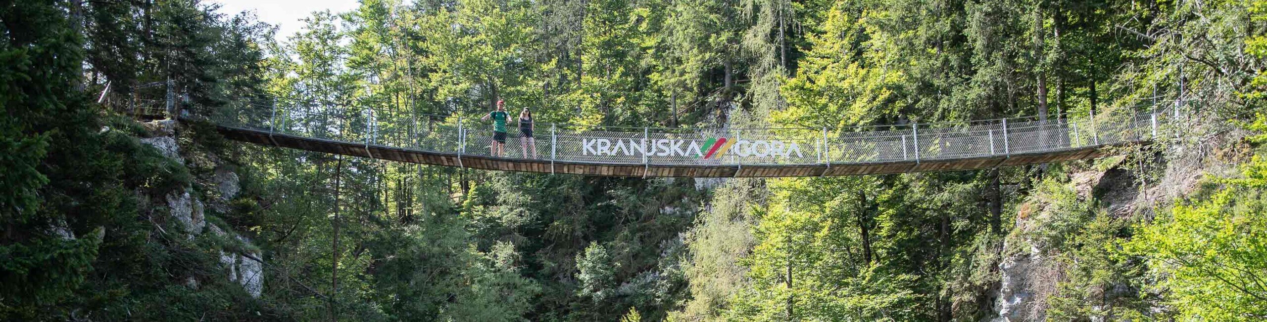 Kranjska Gora ponte sopra la cascata Persone attraversano un ponte sospeso su una cascata a Kranjska Gora, circondata da un paesaggio montano.