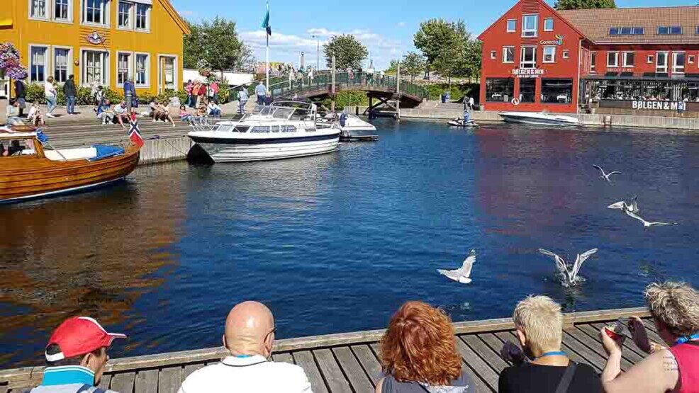 Kristiansand-insenatura del porticciolo con barche attraccate e turisti seduti sulle panchine.
