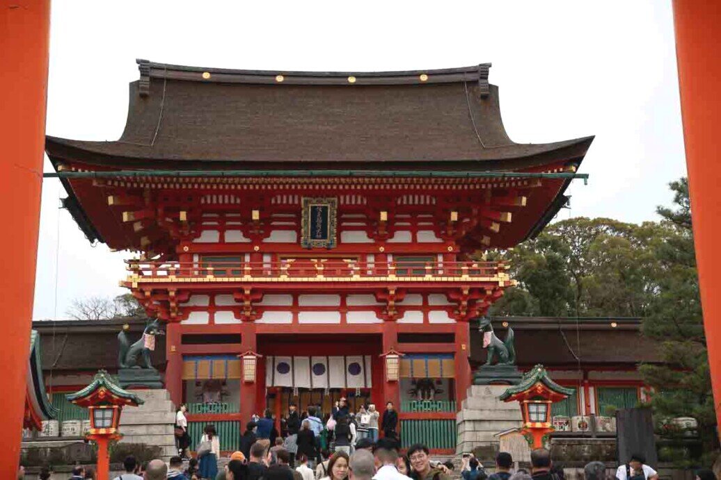 La porta Romon, attraverso la quale si accede al complesso di Fushimi Inari-Taisha Una grande struttura rossa con tetto spiovente e tanta gente attorno.