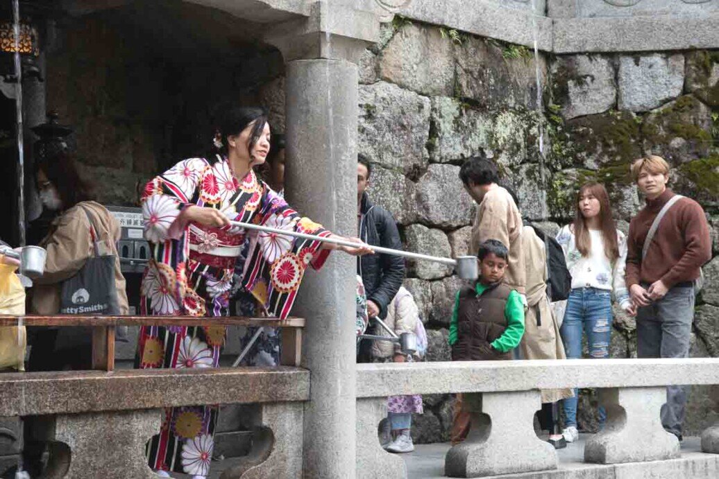 La cascata sacra di Otowa-no-taki Donna in kimono tradizionale che cerca di raccogliere acqua sacra da una piccola cascata con un recipiente collegato ad un'asta.