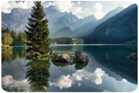Un lago con due grosse pietr in primo piano con sullo sfondo le montagne che si riflettono sul lago di Fusine.