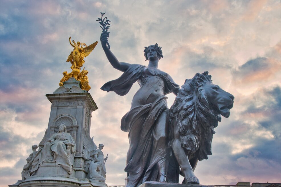 Una statue color oro della regina Vittoria e un'altra in primo piano di un angelo in groppa ad un leone.