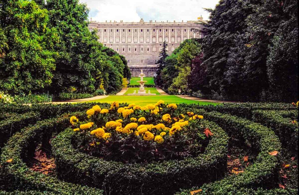 Palazzo Reale di Madrid visto dal giardino, con aiuole fiorite in primo piano.