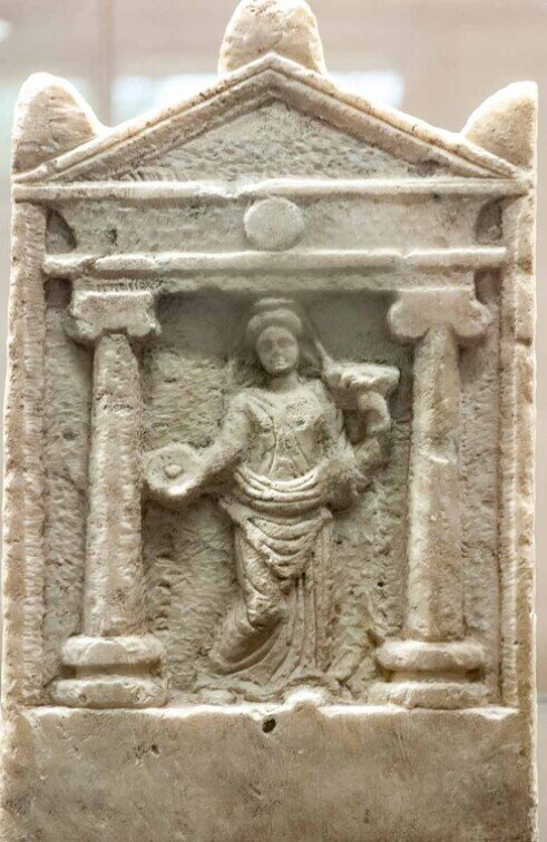 Stele votiva con figura femminile stante entro un’edicola templare.